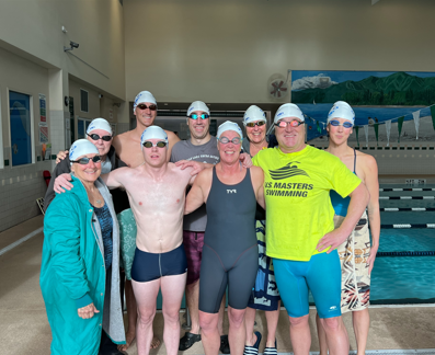 Nine swimmer in gray swim caps linking arms and smiling while standing in front of the Kalispell pool.