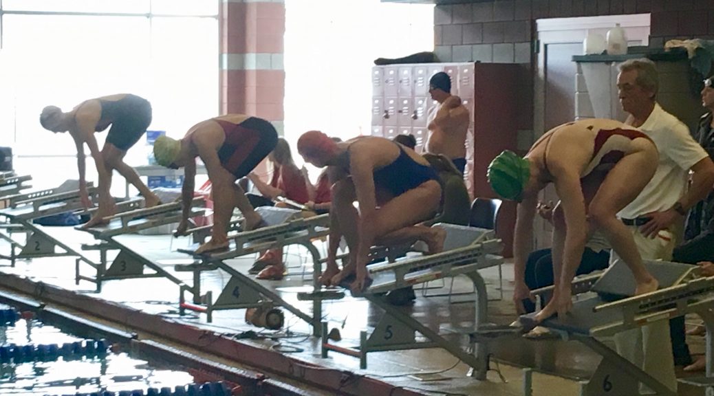 Four swimmers set on the block ready to dive into the crisp indoor pool.
